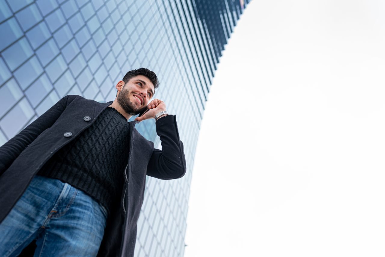 confident and successful young businessman calling with smart phone, blurred financial skyscraper
