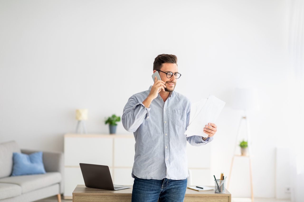 Home office concept. Confident millennial entrepreneur talking on cellphone and discussing financial